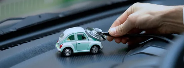 Tablero de auto con un auto de juguete celeste y una mano sosteniendo un la maguera de un estetoscopio