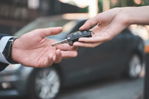 Entrega de llave de auto a otra persona y de fondo un auto