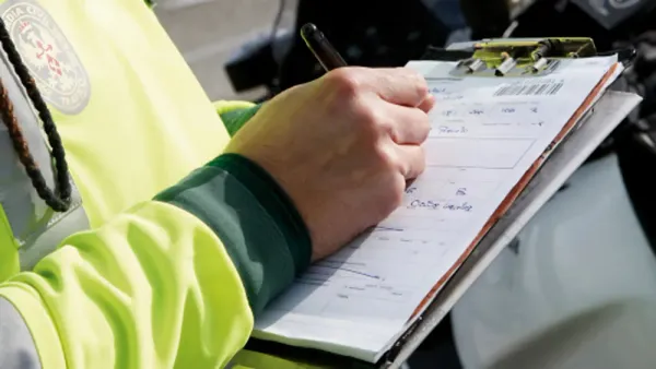 Persona con uniforme de transito llenando un formulario de papel con bolígrafo 