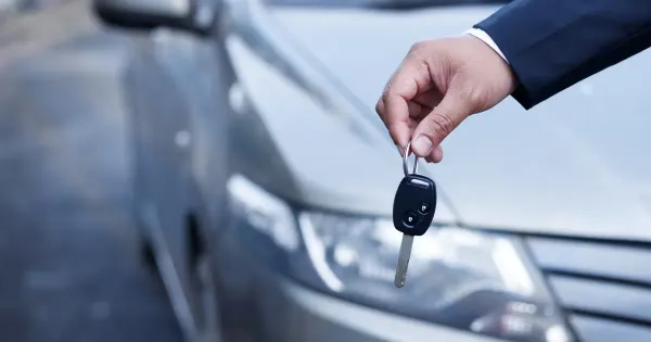 Mano sosteniendo llave de auto y de fondo un auto plateado