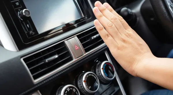 Mano frente a rejillas de aire del tablero de un auto