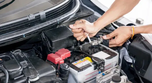 Manos desmontando bornes de batería de auto