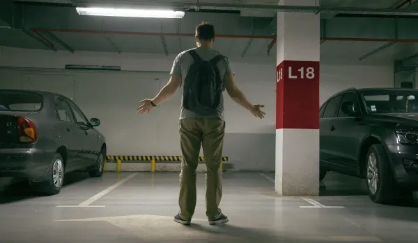 Persona parada con brazo abiertos frente a un lugar de estacionamiento de auto vacío 