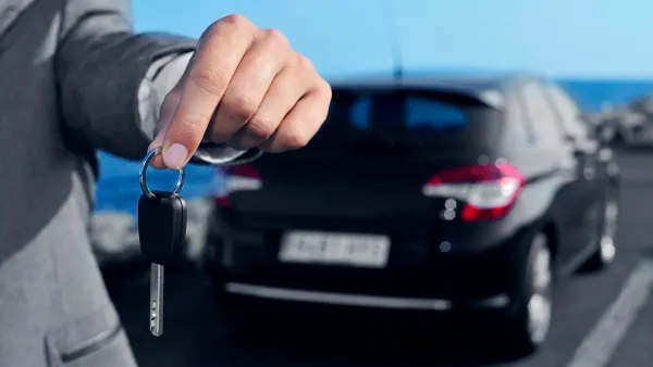 Persona entregando llaves de auto y al fondo un auto negro