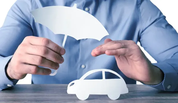 Mano sosteniendo paraguas de papel sobre auto de papel en una mesa