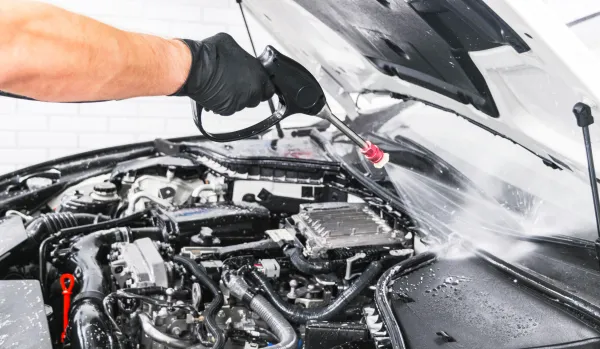 Mano sosteniendo pistola de agua sobre para brisas de auto