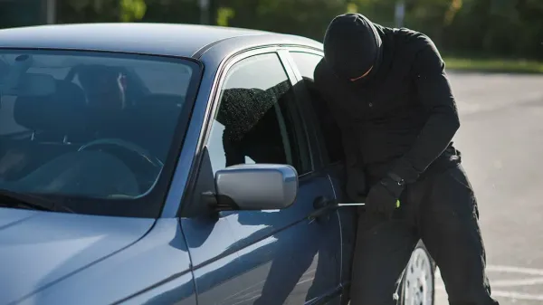 Persona con Capucha y Pasamontañas Forzando Cerradura de Auto Azul con Destornillador 