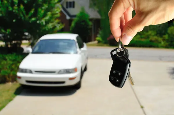 Mano sosteniendo llaves y al fondo un auto blanco